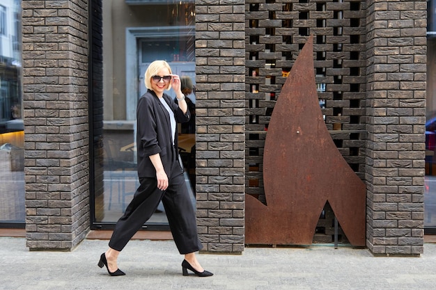 Belle jeune femme blonde portant un costume et marchant dans la rue Une femme vêtue d'un style d'affaires se promène dans la ville