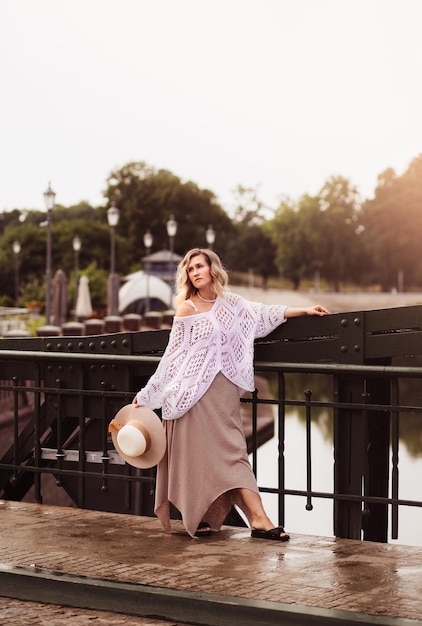 Belle jeune femme blonde portant une robe et un chapeau de paille profitant du lever du soleil sur le front de mer dans la vieille ville européenne Mode et style Voyage d'été