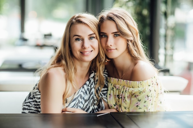 Une belle jeune femme blonde et sa mère se reposent sur une terrasse de café d'été