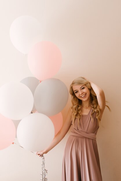 Belle jeune femme blonde souriante avec des ballons blancs gris et roses