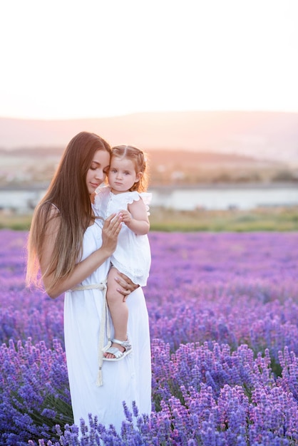 Belle jeune femme blonde tenant une petite fille debout dans un champ de fleurs de lavande en fleurs en plein air