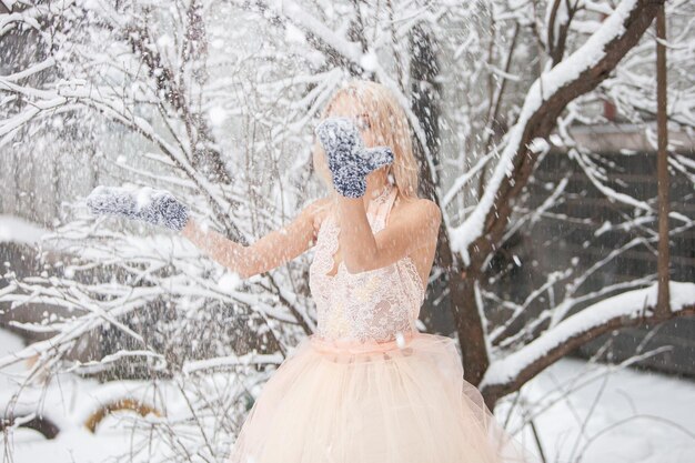 Une belle jeune femme blonde vêtue d'une robe blanche posant dans un parc d'hiver enneigé. Mise au point douce. Mise au point sélective