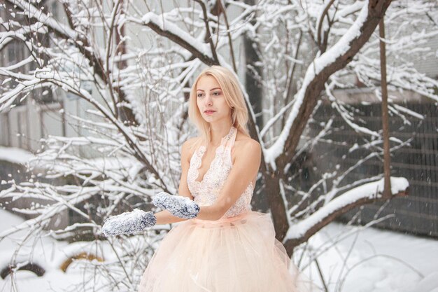 Une belle jeune femme blonde vêtue d'une robe blanche posant dans un parc d'hiver enneigé. Mise au point douce. Mise au point sélective