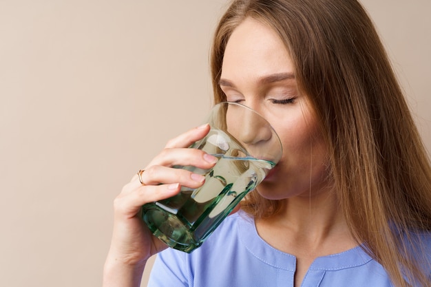 Belle jeune femme en bonne santé buvant de l'eau dans un verre sur fond beige