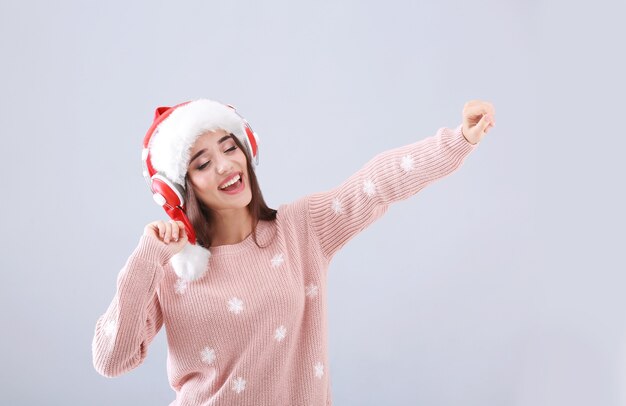 Belle jeune femme en bonnet de Noel écoutant de la musique de Noël sur fond clair