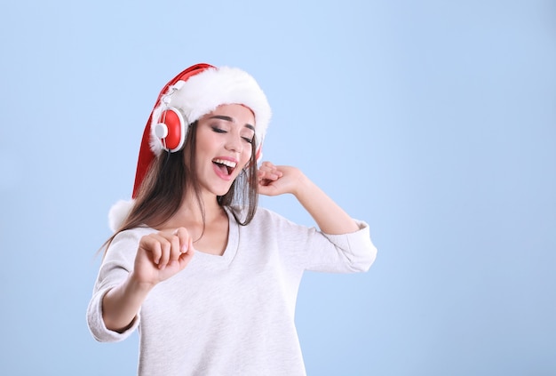 Belle jeune femme en bonnet de Noel écoutant de la musique de Noël sur fond de couleur