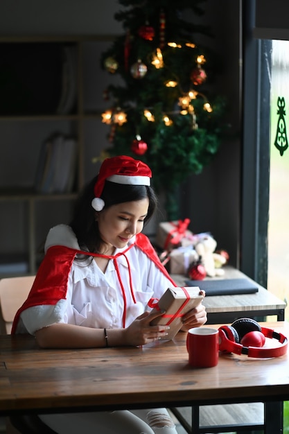 Belle jeune femme en bonnet de Noel tenant une boîte-cadeau de Noël alors qu'elle était assise près de l'arbre de Noël.