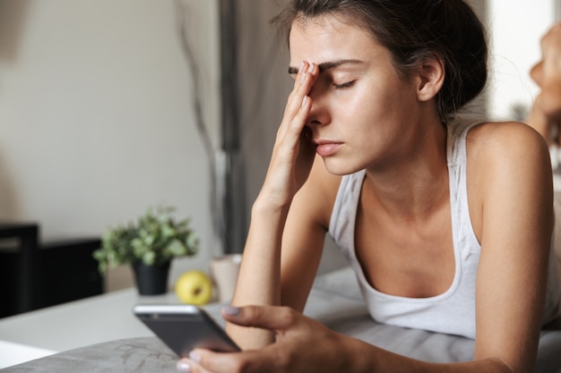 Belle jeune femme bouleversée portant sur un canapé à la maison, à l'aide de téléphone mobile