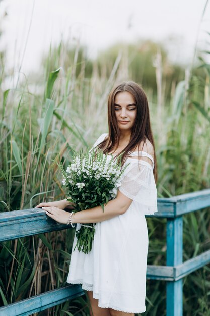 Photo belle jeune femme avec un bouquet de fleurs sauvages avec du maquillage en plein air