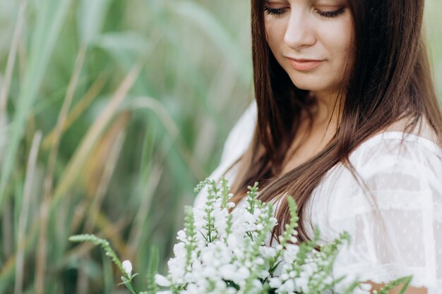 Belle jeune femme avec un bouquet de fleurs sauvages avec du maquillage en plein air