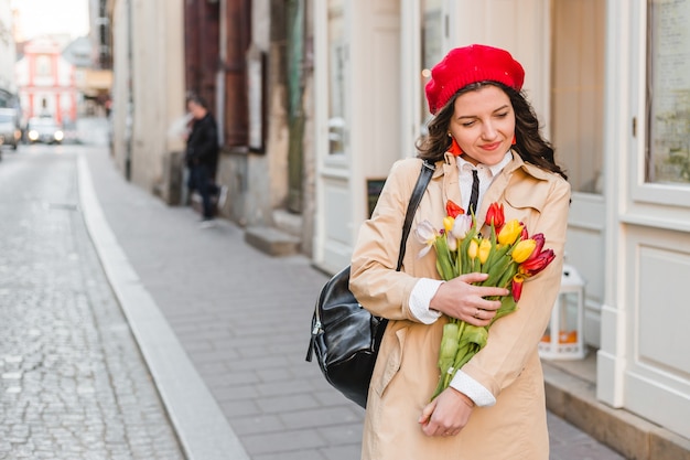 Belle jeune femme avec bouquet de fleurs de tulipes de printemps à la rue de la ville. Fille heureuse qui marche à l'extérieur. Portrait de printemps de jolie femme dans la vieille ville