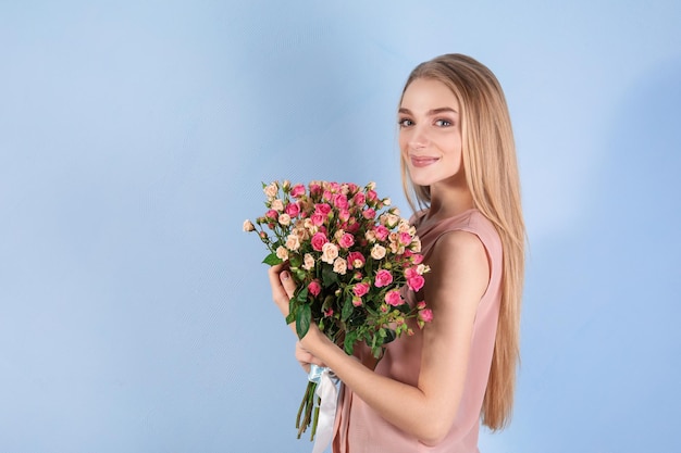 Belle jeune femme avec bouquet de roses sur fond de couleur