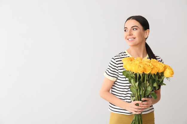 Belle jeune femme avec bouquet de roses sur une surface grise