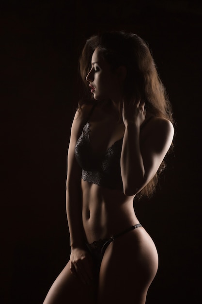 Belle jeune femme bronzée avec un corps sexy qui pose en lingerie dentelle. Ombre et lumière