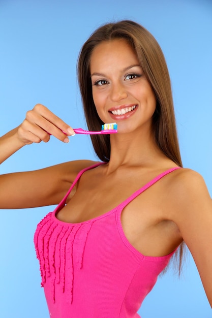 Belle jeune femme avec une brosse à dents sur fond bleu