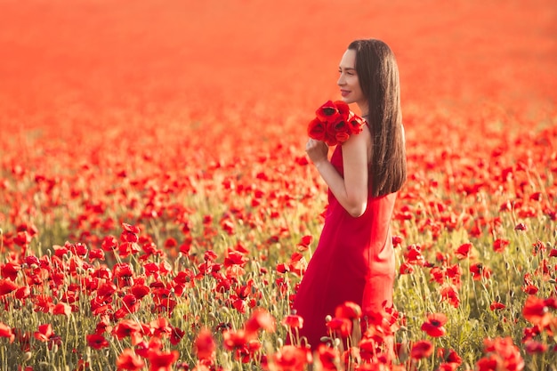 Belle jeune femme brune aux longs cheveux coiffés en robe rouge profiter d'un champ de coquelicots