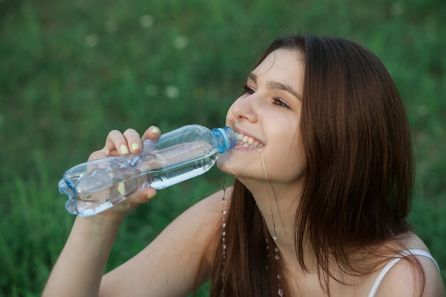 Belle jeune femme brune buvant de l'eau à partir d'une bouteille dans un parc