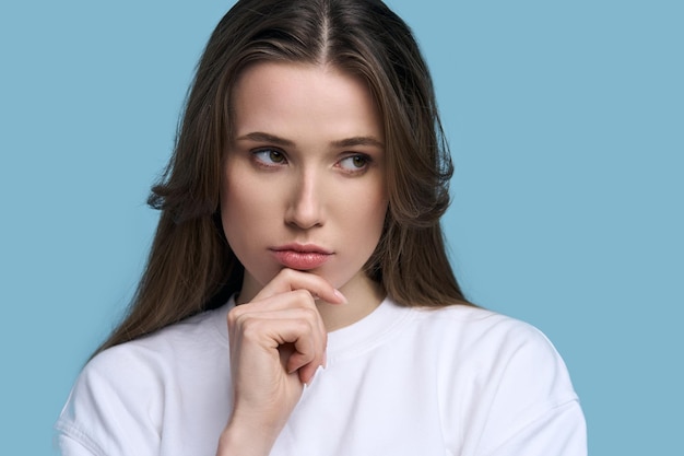 Belle jeune femme brune caucasienne à la recherche de lèvres boudeuses pensives isolées sur fond bleu