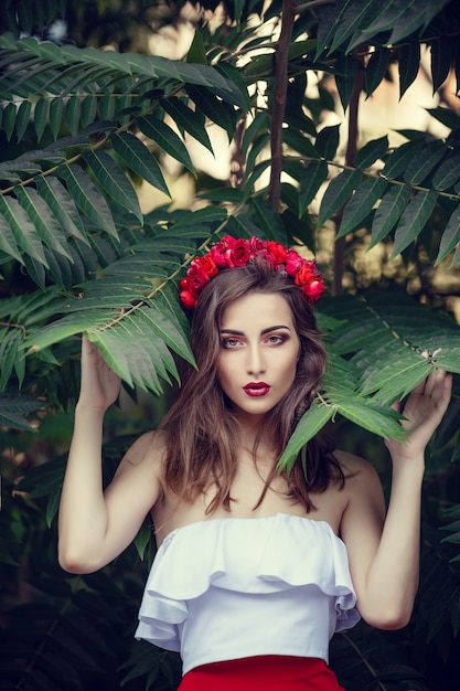 Belle jeune femme brune dans un parc au coucher du soleil avec une couronne de fleurs