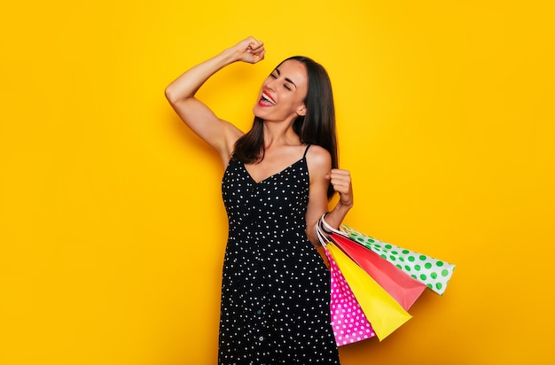 Belle jeune femme brune élégante et heureuse dans une robe pose avec de nombreux sacs à provisions colorés et s'amuse