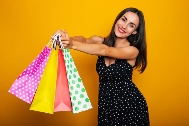 Belle jeune femme brune élégante et heureuse dans une robe pose avec de nombreux sacs à provisions colorés et s'amuse