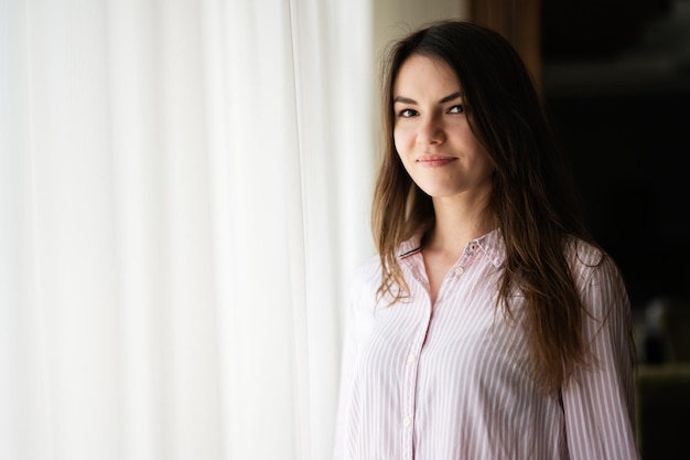 Belle jeune femme brune à la fenêtre fond clair