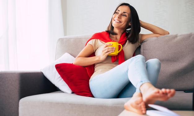 Belle jeune femme brune heureuse se détend sur le canapé à la maison et rêve