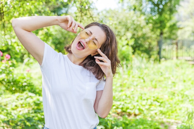 Belle jeune femme brune en lunettes de soleil jaunes à la mode au repos et souriant dans le parc