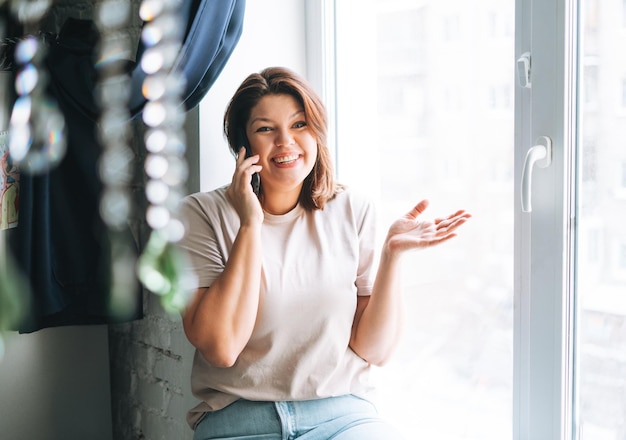 Belle jeune femme brune plus le corps de taille positive parlant par téléphone portable à la maison