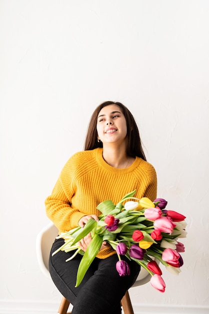 Belle jeune femme brune en pull jaune avec bouquet de tulipes roses fraîches
