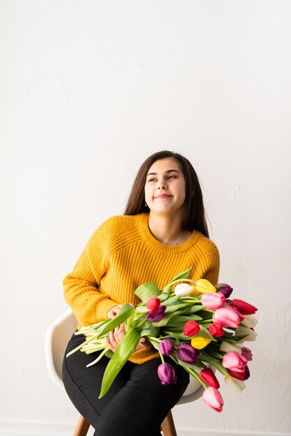 Belle jeune femme brune en pull jaune avec bouquet de tulipes roses fraîches