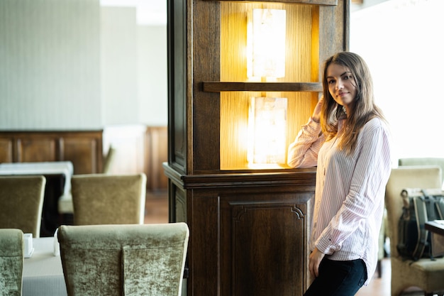 Belle jeune femme brune se tient au restaurant près de la colonne avec des lumières