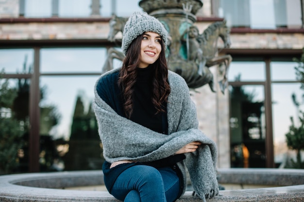 Belle jeune femme brune souriante naturelle portant un chandail tricoté, des gants en cuir, une écharpe et un chapeau Couvert de flocons de neige Concept de mode automne et hiver