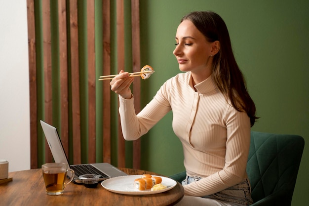 Photo une belle jeune femme brune vêtue d'un sweat-shirt beige mange des rouleaux de sushi avec des baguettes dans le