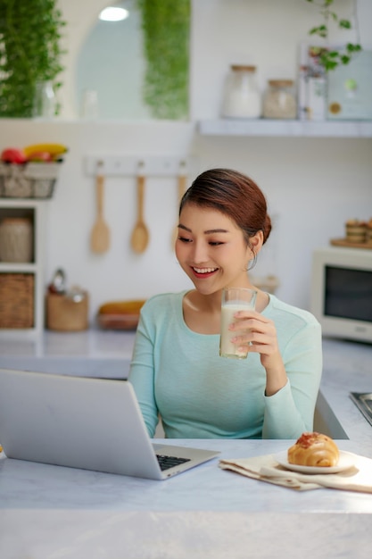 Belle Jeune Femme Buvant Un Délicieux Smoothie Sain Et Utilisant Un Ordinateur Portable à La Maison