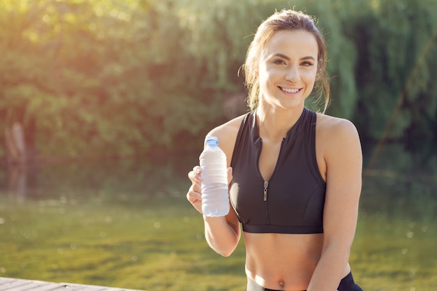 Belle jeune femme buvant de l'eau pendant le jogging matinal dans le parc