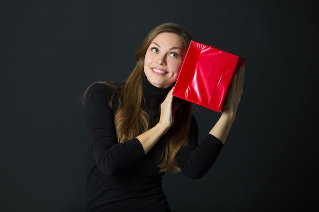 Belle jeune femme avec un cadeau à la main sur fond noir