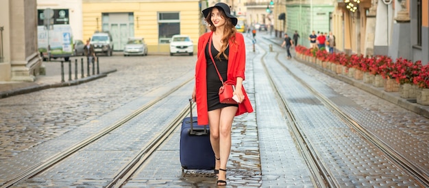 Belle jeune femme caucasienne marche avec une valise sur une voie de tramway humide dans la ville européenne