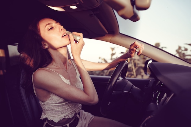 Belle jeune femme caucasienne peignant des lèvres sur le siège avant de sa voiture