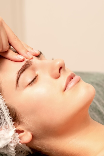 Belle jeune femme caucasienne recevant un massage du visage avec les yeux fermés dans le salon spa close up Concept de traitement relaxant
