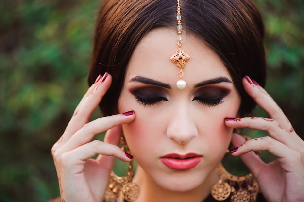 Belle jeune femme caucasienne en sari indien traditionnel avec maquillage et bijoux de mariée et tatouage au henné sur les mains