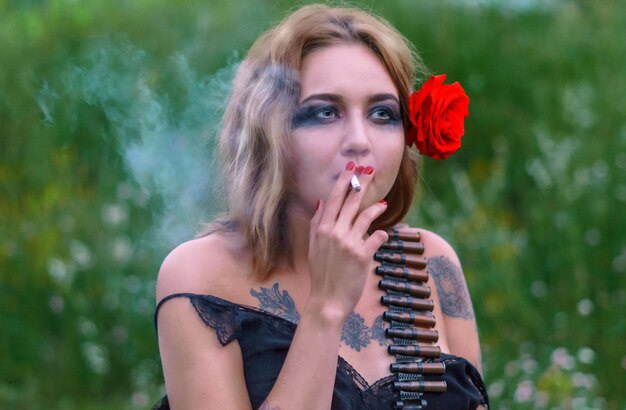 Photo une belle jeune femme avec une ceinture de cartouche fumant une cigarette