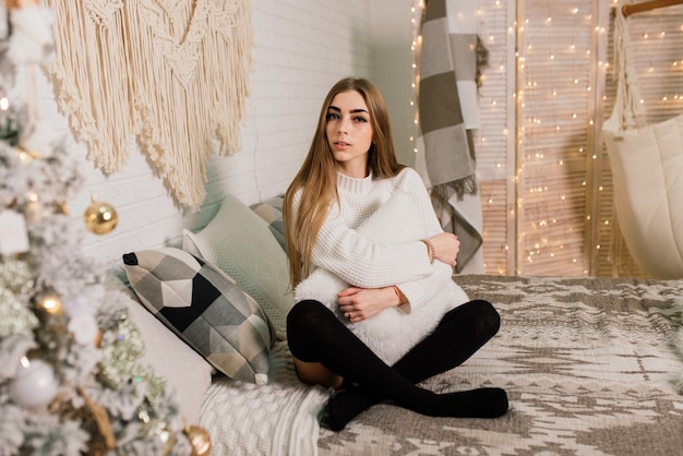 Belle jeune femme célébrant Noël à la maison, s'amusant en ouvrant des cadeaux