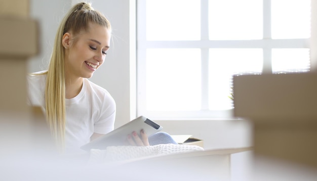 Une belle jeune femme célibataire déballant des cartons et emménageant dans une nouvelle maison Une femme regarde ici la tablette