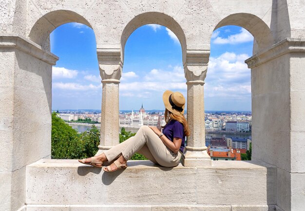 Belle jeune femme avec un chapeau assis sur le mur en regardant le magnifique paysage urbain de Budapest Hongrie