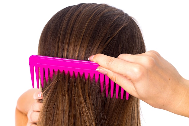 Belle jeune femme en chemise colorée peignant ses longs cheveux têtus à l'aide d'une brosse à cheveux rose