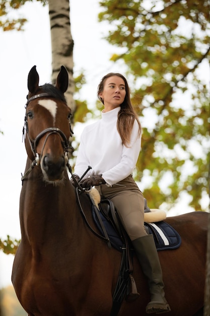 Belle jeune femme avec cheval en plein air Concept de soins aux animaux Repos rural et loisirs Idée de tourisme vert Jeune femme européenne portant l'uniforme