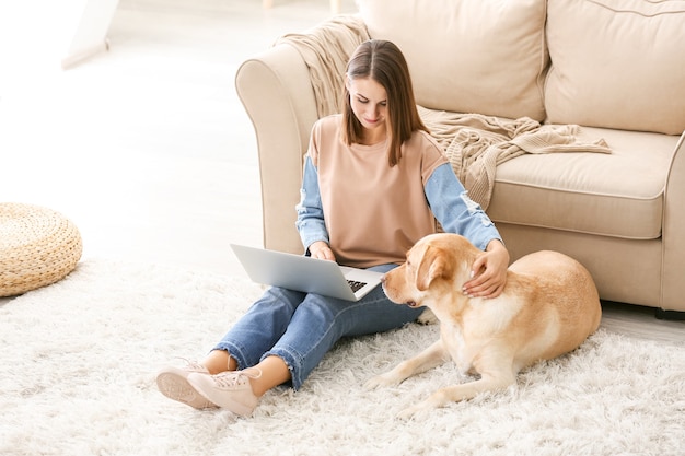 Belle jeune femme avec un chien mignon utilisant un ordinateur portable à la maison