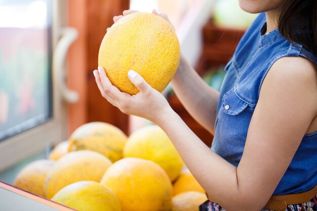 Belle jeune femme choisit des melons dans un magasin de légumes