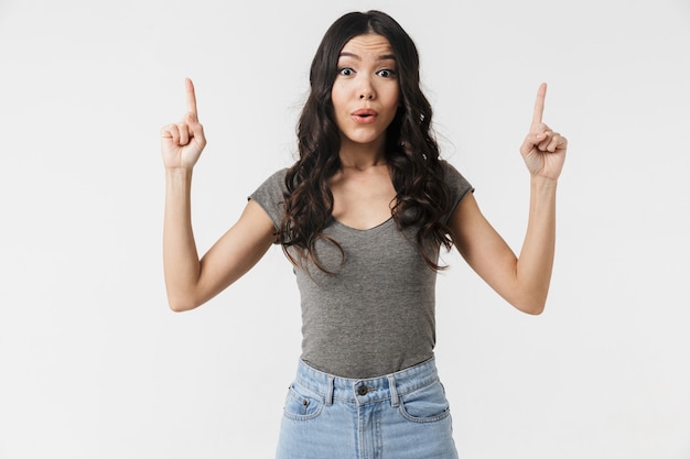 une belle jeune femme choquée posant isolée sur un mur blanc pointant.